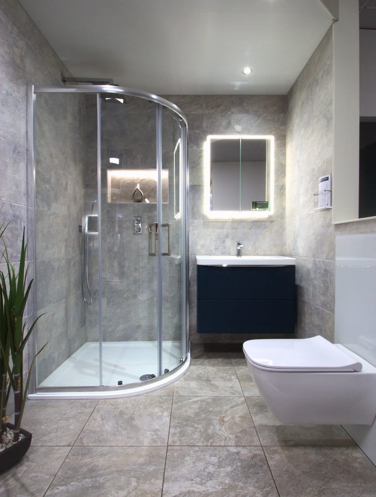 Luxury bathroom in Hillington, Glasgow, with a curved glass shower enclosure, floating vanity with a backlit mirror, and grey marble-effect wall tiles for a sophisticated ambiance.