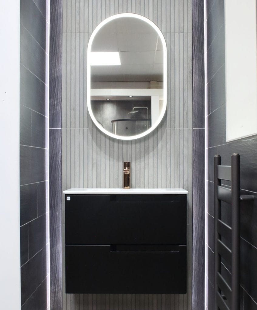 Minimalist bathroom in Glasgow with dark grey wall tiles, a floating vanity with a sleek, oval backlit mirror, creating a contemporary look ideal for compact spaces.