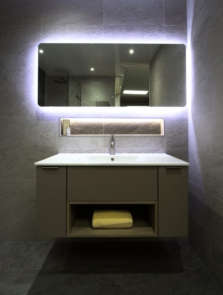 Modern bathroom in Glasgow featuring a floating vanity with a built-in towel shelf, a large rectangular backlit mirror, and sleek grey tiles for a refined, minimalist look.