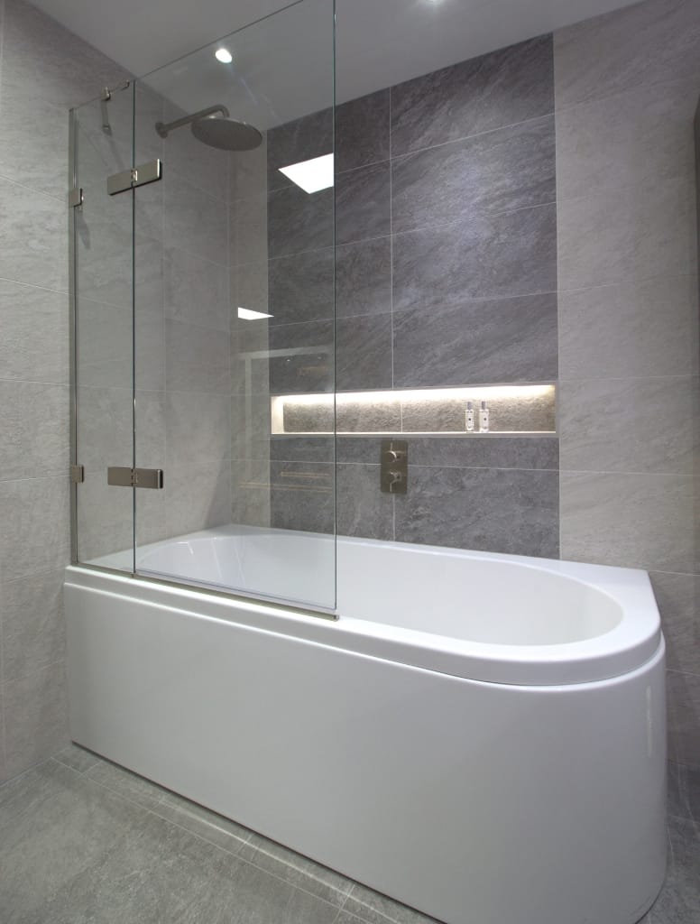 Luxury Shower bath with a glass shower screen and wall-mounted rain shower head, surrounded by grey textured tiles in a high-end Glasgow bathroom.