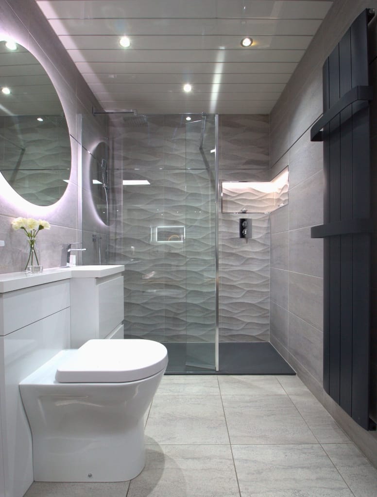 Minimalist bathroom in Glasgow with wave-textured wall tiles from Porcelanosa, a round backlit mirror, and a sleek black towel radiator, achieving a clean, modern aesthetic.