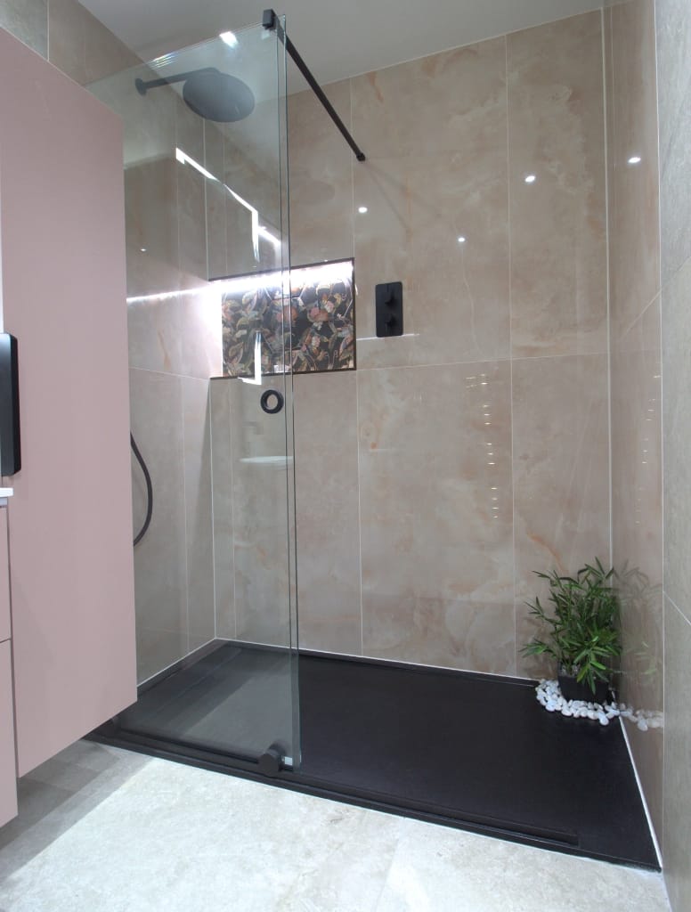 Modern walk-in shower in Hillington, Glasgow, featuring beige marble-effect wall tiles, black fixtures, and a decorative inset with botanical patterns for a touch of elegance.