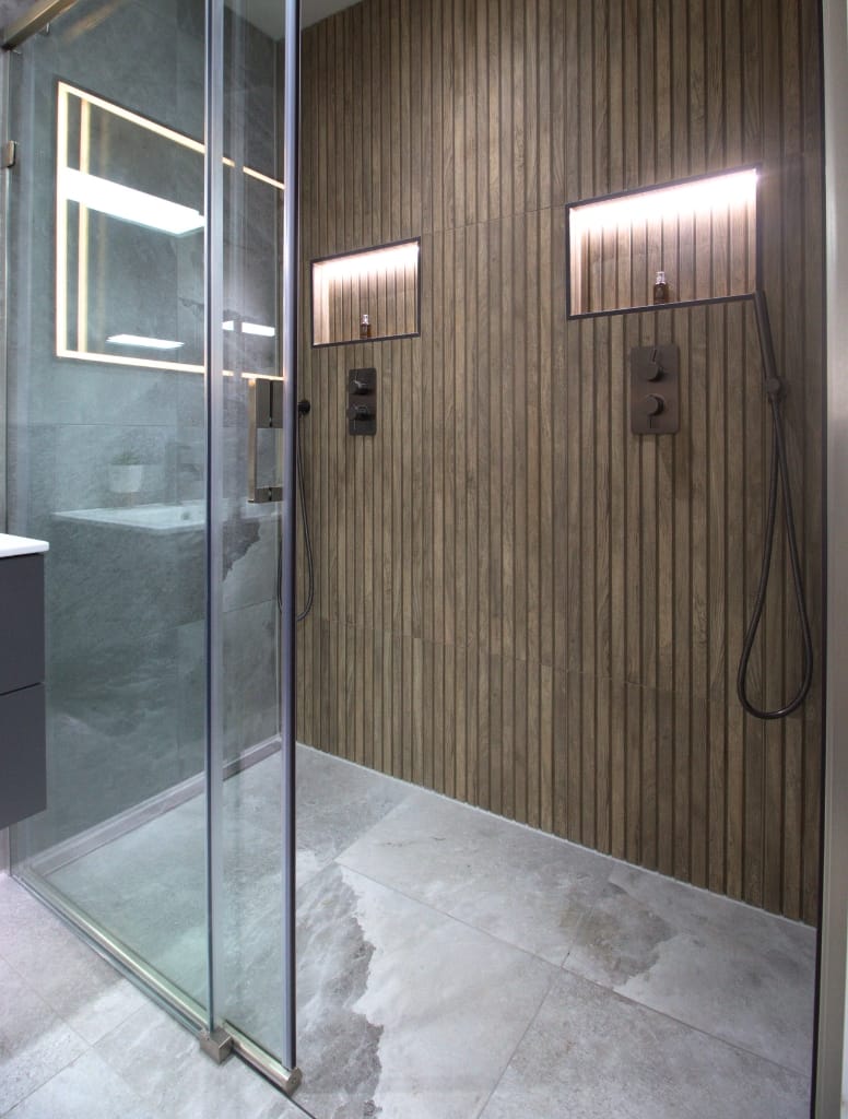 Bright, contemporary bathroom in Glasgow with a curved glass shower enclosure, dark towel rail, floating vanity, and textured grey wall tiles, combining style with functionality.